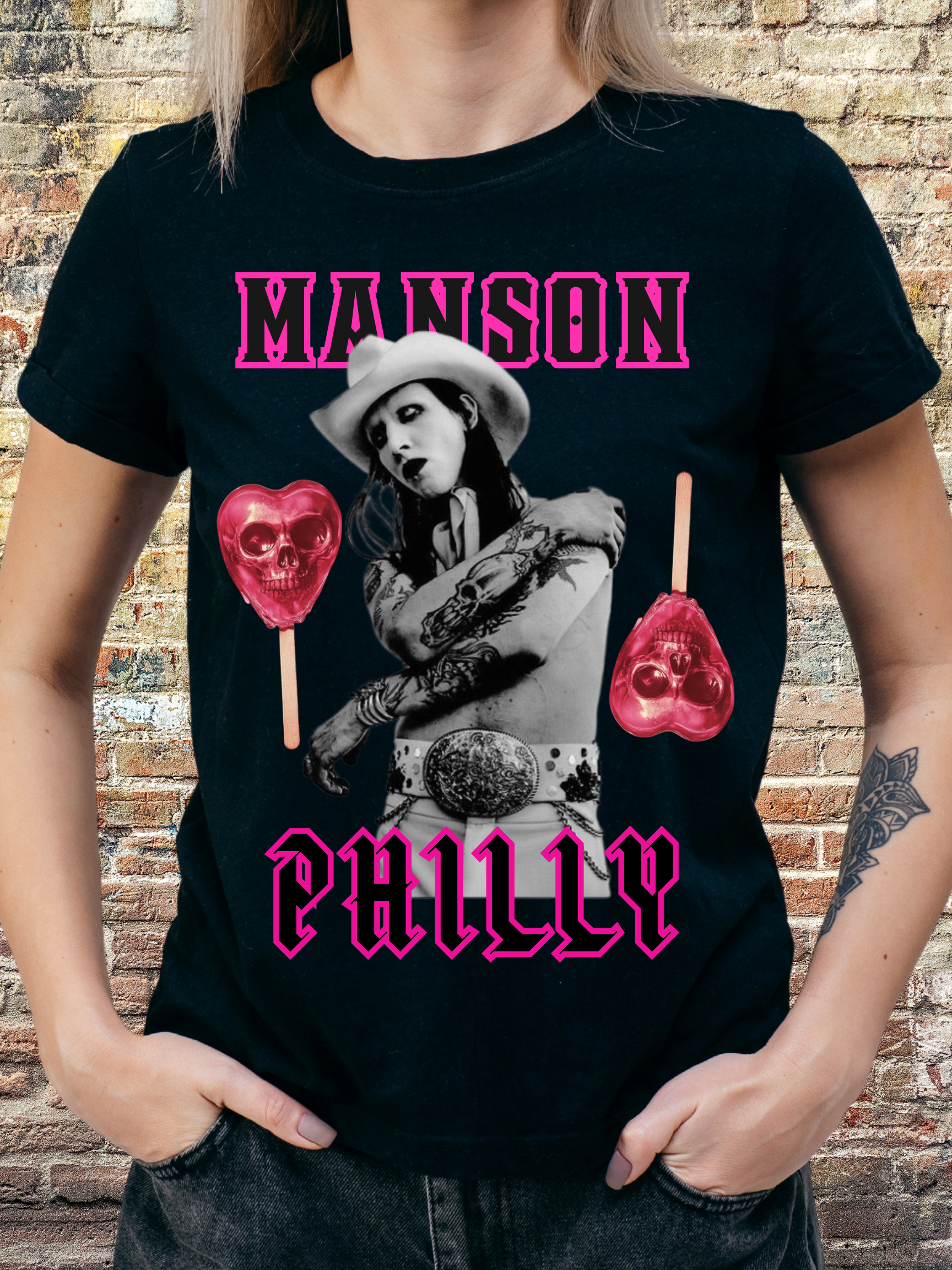 Black t-shirt with a bold gothic western theme featuring a monochrome figure in a cowboy hat, pink skull lollipops, and the words "Manson Philly" in hot pink Old English-style font